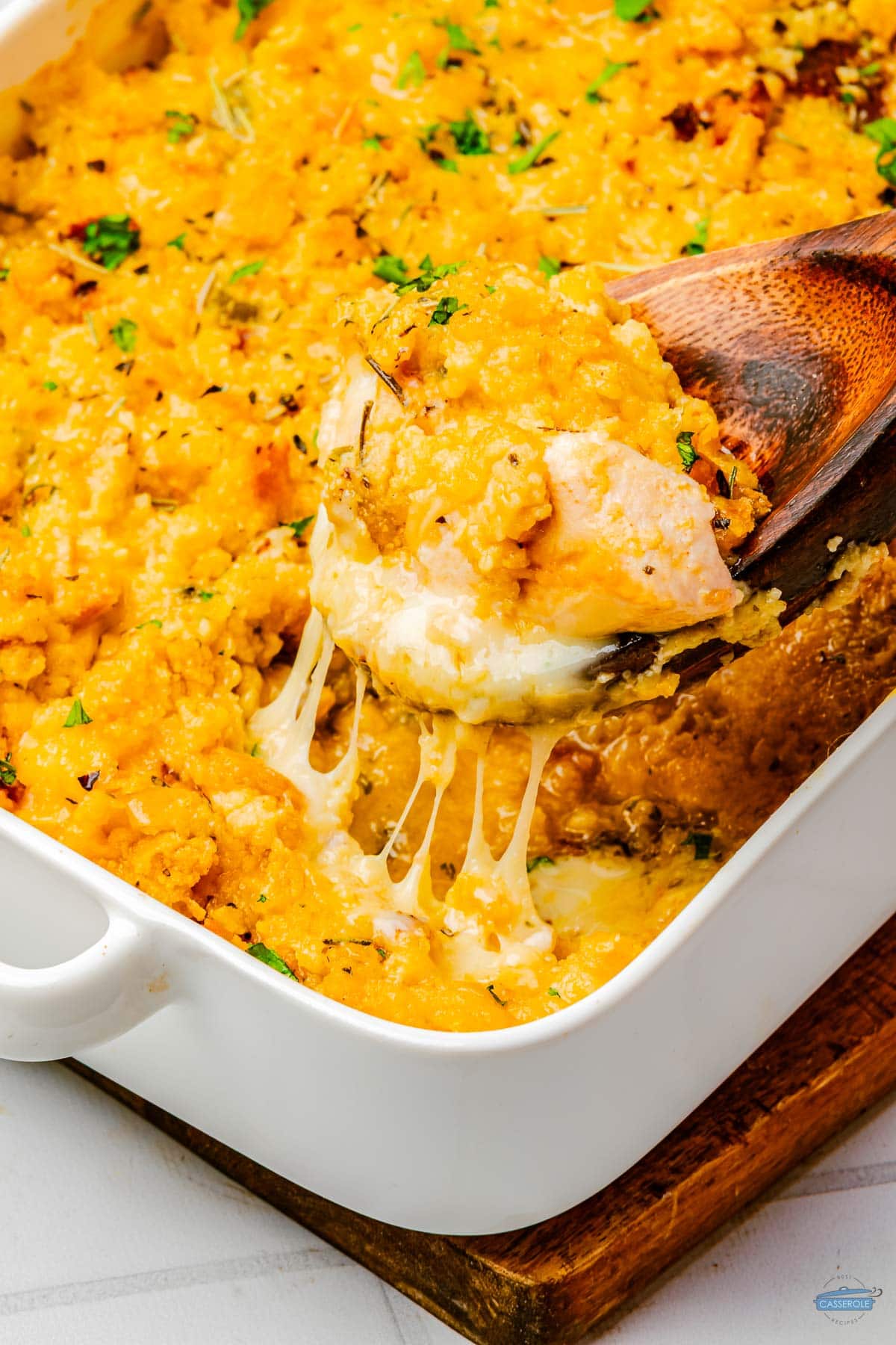 scoop of chicken casserole on a wood spoon above a white dish